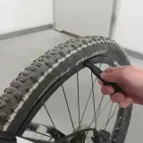Dłoń z łyżką do opon pomaga założyć oponę rowerową, dbając o prawidłowy kierunek bieżnika.