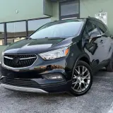 Czarny Buick Encore lśni w słońcu, zaparkowany przed zielonym budynkiem.