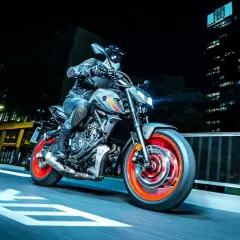Motocyklista na szarym Yamaha MT-07 z pomarańczowymi felgami pędzi nocą przez miasto. Dane techniczne tego modelu są imponujące.