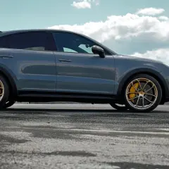 Szary Porsche Cayenne Turbo GT z żółtymi zaciskami hamulcowymi na złotych felgach, zaparkowany na pustej drodze z górzystym krajobrazem w tle.