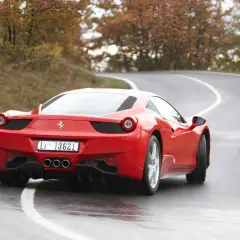 Czerwone Ferrari 458 na mokrej, krętej drodze wśród jesiennych drzew.