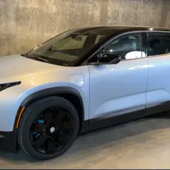 Srebrny elektryczny SUV Fisker Ocean z czarnym dachem i czarnymi felgami stoi na betonowym podłożu.