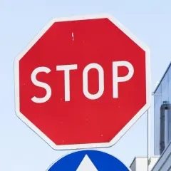 Czerwony znak stop z białym napisem "STOP" na tle nieba i budynku.