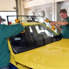 Dwóch mechaników montuje przednią szybę w żółtym samochodzie. Sprawdź autoglass cennik usług.