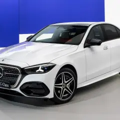 Biały sedan marki Daimler, nowy C-Klasa, prezentuje się elegancko na tle niebieskiego logo.