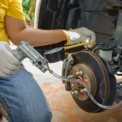 Mechanik w żółtej koszulce i rękawiczkach wykonuje odpowietrzanie hamulców za pomocą specjalnego narzędzia z manometrem.