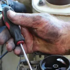 Brudna ręka mechanika przykręca śrubę, kontynuując wymianę linki hamulca ręcznego.