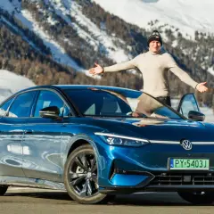 Mężczyzna z otwartymi ramionami stoi obok lśniącego, niebieskiego VW ID.7 na tle ośnieżonych gór.