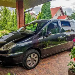 Czarny Citroen C8 zaparkowany pod zadaszeniem, otoczony zielenią i domami z czerwonymi dachami.
