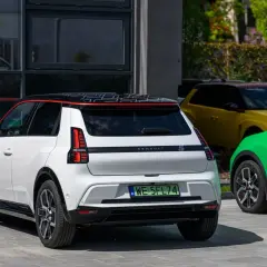 Biały Renault 5 e-tech z czarnym dachem i czerwonymi akcentami stoi obok zielonego i żółtego samochodu.