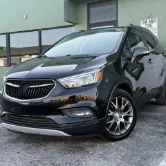 Czarny Buick Encore lśni w słońcu, zaparkowany przed zielonym budynkiem.