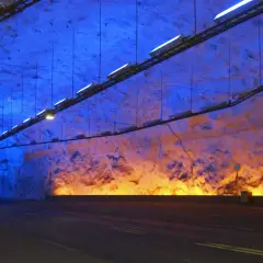 Wnętrze najdłuższego tunelu na świecie, oświetlone niebieskim i pomarańczowym światłem, z drogą prowadzącą w mrok.
