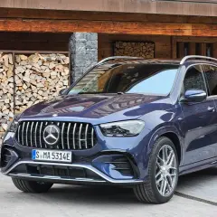 Elegancki, granatowy Mercedes GLE 53 AMG zaparkowany przed drewnianym domem z ułożonym drewnem.