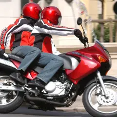 Dwie osoby w kaskach i kurtkach jadą na czerwonym motocyklu. To idealny sposób na zdobycie prawa jazdy na motor 125.