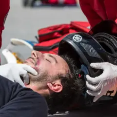 Ratownik w czerwonym stroju z grecką flagą pomaga poszkodowanemu motocykliście. Borkoś ma siniaka pod okiem.