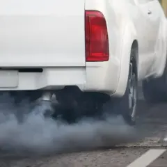 Biały dym wydobywa się z rury wydechowej białego pickupa, który przyspiesza na drodze.