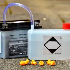 Akumulator motocyklowy i kanister z płynem, obok pomarańczowe zatyczki. Różne rodzaje akumulatorów wymagają odpowiedniej pielęgnacji.