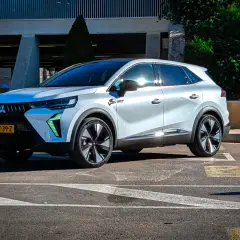 Nowy Mitsubishi Grandis w białym kolorze, zaparkowany na parkingu przed budynkiem.