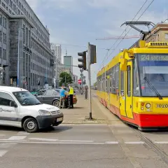 Żółty tramwaj z numerem 24 Gocławek ma pierwszeństwo na skrzyżowaniu, podczas gdy policjanci rozmawiają z kierowcą białego vana.