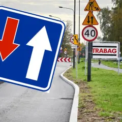 Znak D5 z białymi strzałkami, jedna w górę, druga w dół, na niebieskim tle. Obok znaki drogowe i tablica "TRABAG".