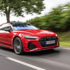 Czerwony Audi RS7 Sportback pędzi po drodze, otoczony zielenią drzew.
