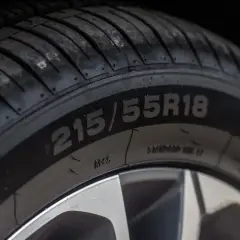 Zbliżenie na oponę z widocznym rozmiarem 215/55R18. Na boku opony można dostrzec oznaczenia dotyczące daty produkcji opony.