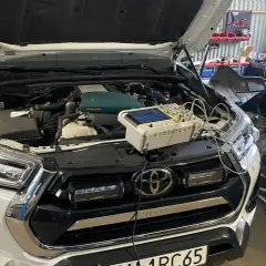 Biały Toyota Land Cruiser Prado w warsztacie, z otwartą maską i podłączonym sprzętem diagnostycznym.
