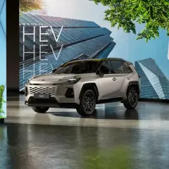 Srebrny SUV z napisem HEV na tle nowoczesnych budynków i zieleni.
