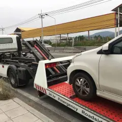 Pomoc drogowa w akcji: białe auto jest ładowane na lawetę. Widać mechanizm, jak holować auto, by bezpiecznie przetransportować pojazd.