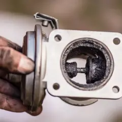 Brudny zawór EGR z nagarem. Ręce mechanika są ubrudzone sadzą po demontażu.