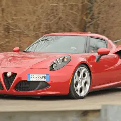 Czerwona Alfa Romeo 4C pędzi po krętej drodze, jej sportowy design przyciąga wzrok.