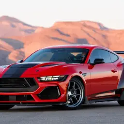 Czerwony Shelby Mustang z czarnymi pasami i spojlerem na tle pustynnych gór.