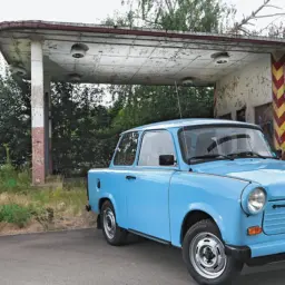 Niebieski trabant stoi przed opuszczoną stacją benzynową.