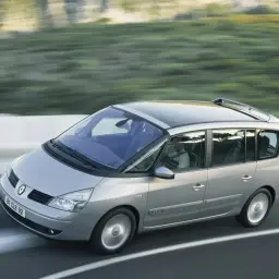 Srebrny Renault Espace 4 z panoramicznym dachem pędzi po drodze, za kierownicą siedzi mężczyzna.