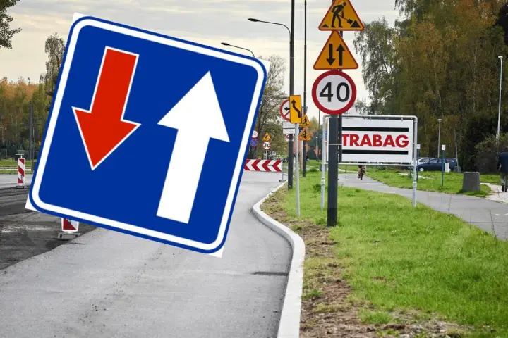 Znak D5 z białymi strzałkami, jedna w górę, druga w dół, na niebieskim tle. Obok znaki drogowe i tablica "TRABAG".