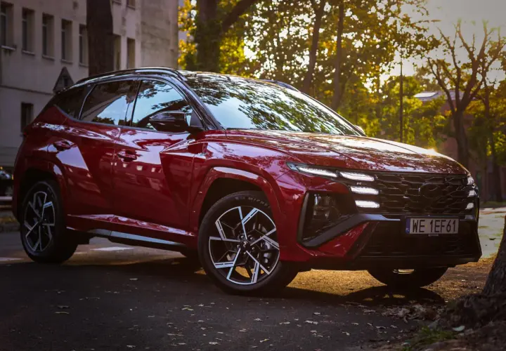 Czerwony Hyundai Tucson hybryda zaparkowany przy ulicy, oświetlony zachodzącym słońcem.