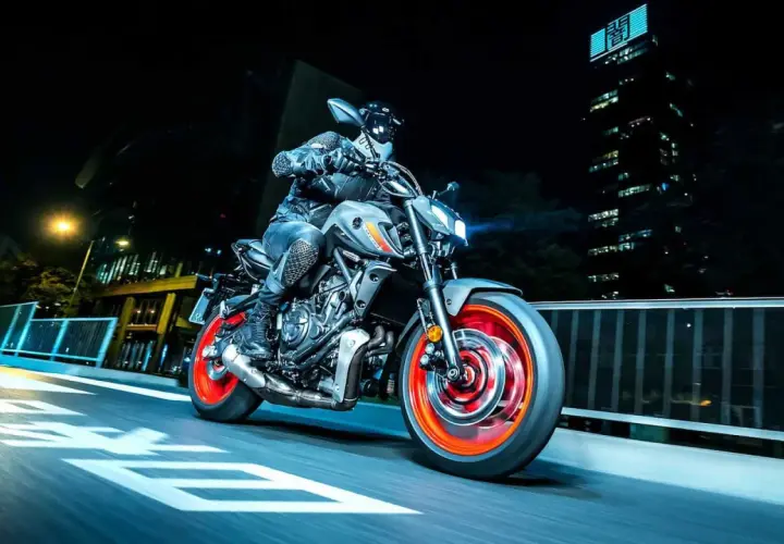 Motocyklista na szarym Yamaha MT-07 z pomarańczowymi felgami pędzi nocą przez miasto. Dane techniczne tego modelu są imponujące.