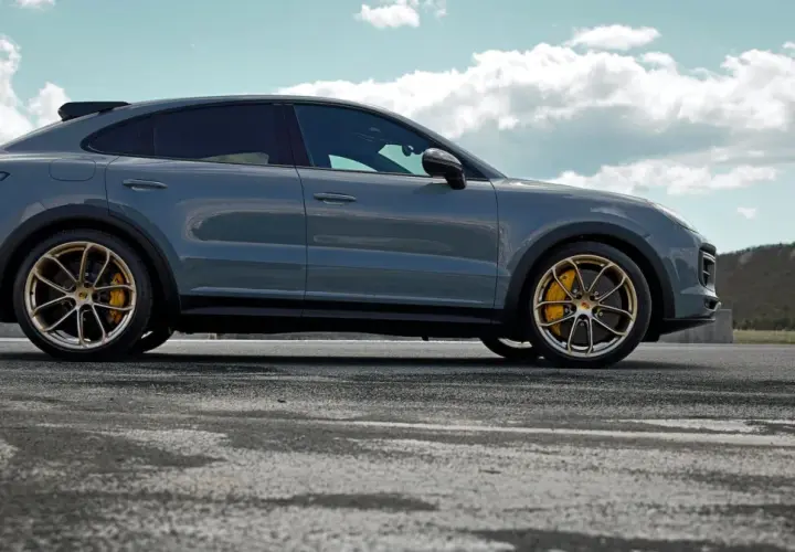 Szary Porsche Cayenne Turbo GT z żółtymi zaciskami hamulcowymi na złotych felgach, zaparkowany na pustej drodze z górzystym krajobrazem w tle.