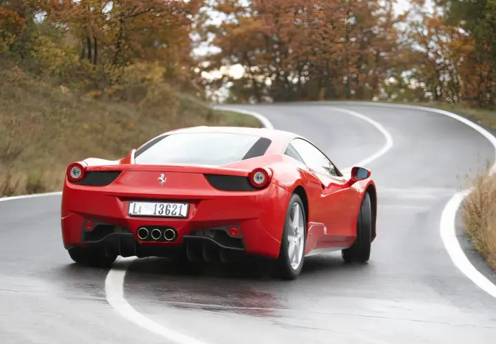 Czerwone Ferrari 458 na mokrej, krętej drodze wśród jesiennych drzew.
