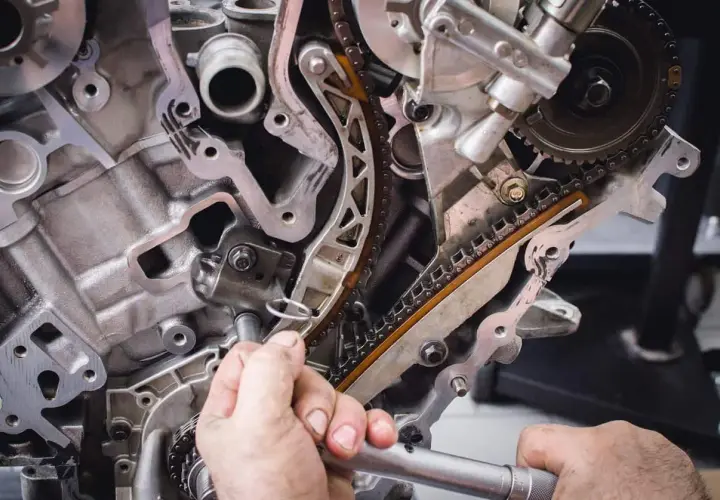 Mechanik pracuje przy rozrządzie silnika. Zbliżenie na łańcuch rozrządu i napinacz. Objawy zużytej poduszki silnika mogą być różne.
