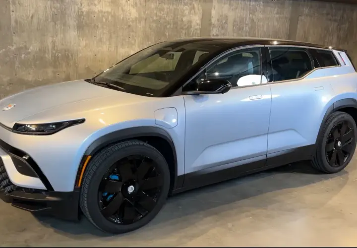 Srebrny elektryczny SUV Fisker Ocean z czarnym dachem i czarnymi felgami stoi na betonowym podłożu.
