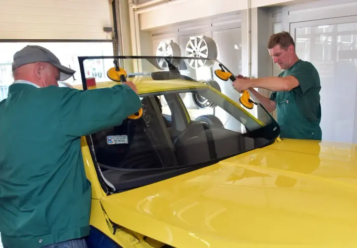 Dwóch mechaników montuje przednią szybę w żółtym samochodzie. Sprawdź autoglass cennik usług.