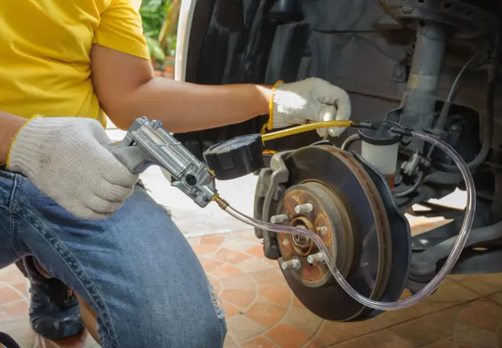 Mechanik w żółtej koszulce i rękawiczkach wykonuje odpowietrzanie hamulców za pomocą specjalnego narzędzia z manometrem.