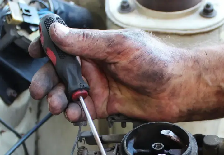 Brudna ręka mechanika przykręca śrubę, kontynuując wymianę linki hamulca ręcznego.