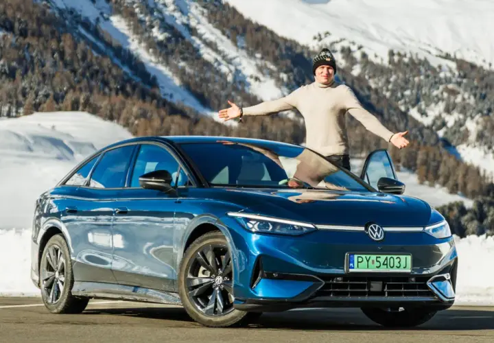 Mężczyzna z otwartymi ramionami stoi obok lśniącego, niebieskiego VW ID.7 na tle ośnieżonych gór.