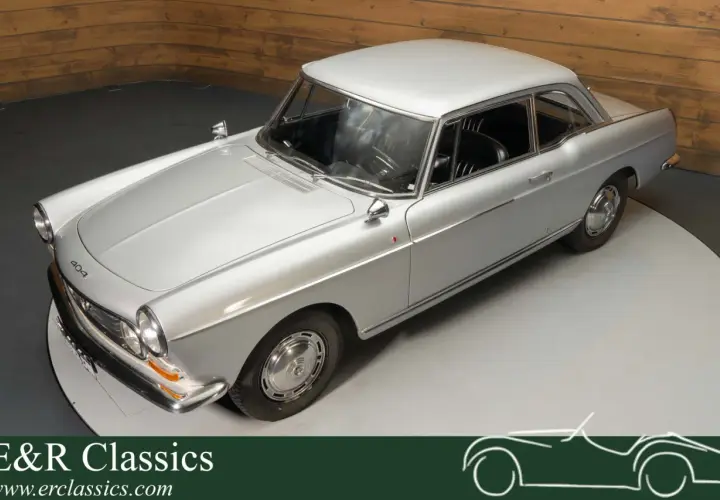 Elegancki, srebrny Peugeot 404 coupe z lat 60. na obrotowej platformie. Klasyka motoryzacji.