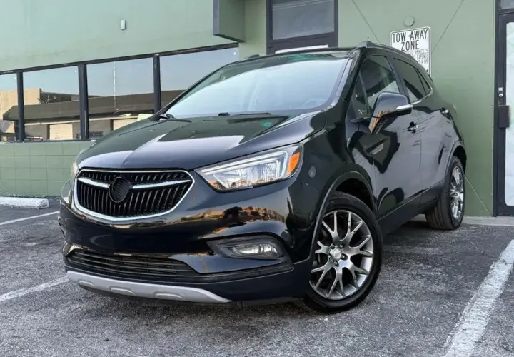 Czarny Buick Encore lśni w słońcu, zaparkowany przed zielonym budynkiem.