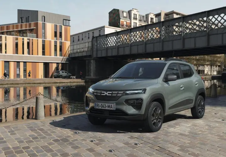 Dacia Spring cena: zielony elektryczny samochód miejski stoi na brukowanej ulicy nad kanałem, w tle nowoczesne budynki i most.
