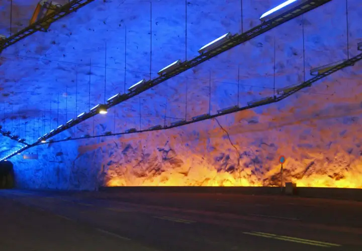 Wnętrze najdłuższego tunelu na świecie, oświetlone niebieskim i pomarańczowym światłem, z drogą prowadzącą w mrok.