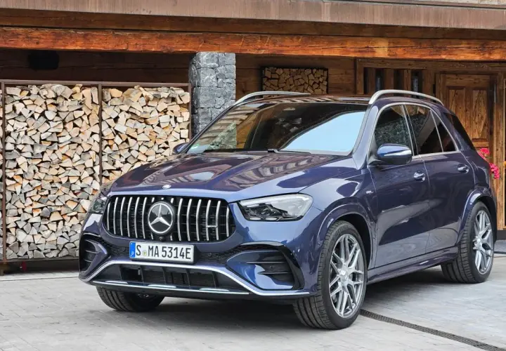 Elegancki, granatowy Mercedes GLE 53 AMG zaparkowany przed drewnianym domem z ułożonym drewnem.